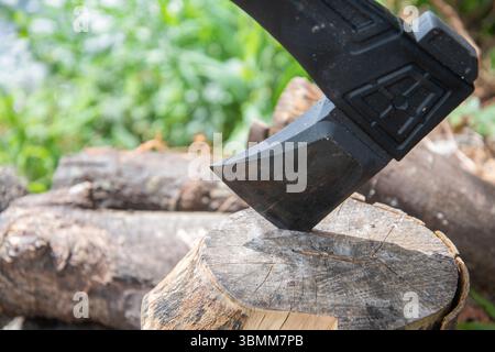 Outdoor-Szene mit einer Axt, die in einem Häckselblock neben einem Holzhaufen eingebettet ist, was auf rustikales Wohnen, Brennholzzubereitung oder Waldarbeiten hindeutet. Stockfoto