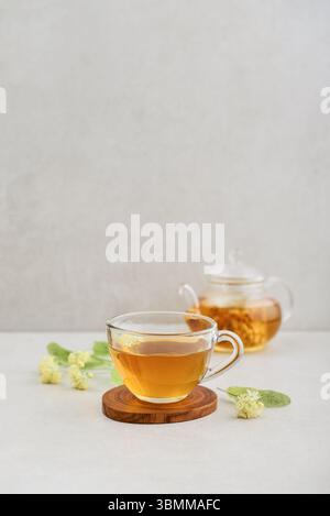 Glasschale Lindentee mit Glas-Teekanne und Lindenblüten auf hellem Hintergrund Stockfoto