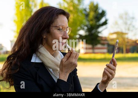 Attraktive Geschäftsfrau mittleren Alters, die draußen Lippenstift auf die Lippen legt Stockfoto
