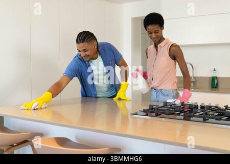 Diverse Pärchen putzen die Küchenarbeitsplatte und den Herd mit Gummihandschuhen ab Stockfoto
