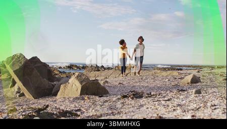 Mann und Frau, die Hände an der felsigen Küste halten, mit Kieselschalen, Meereswellen Stockfoto