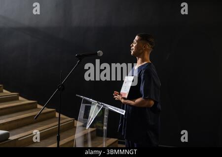 Mann, der neben einem Acrylpult steht und ein Zertifikat hält, mit Mikrofon auf der Bühne, Kopierraum Stockfoto