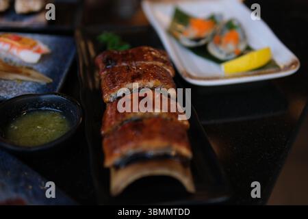 Stilvolles schwarzes Sushi-Set auf einem flachen Teller mit verschiedenen Arten von Rollen, Nigiri, Maki, Gunkan. Japanische nationale Küche aus nächster Nähe. Essstäbchen geräucherter Aal Stockfoto