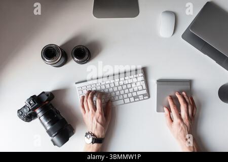 Der Konstrukteur Sitzt Am Arbeitsplatz Und Tippt Auf Der Tastatur. Draufsicht auf Herrenhände und auf Einem Tisch mit Einer Fotokamera mit Objektiven für Kamera mit Stockfoto