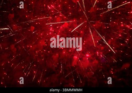 Intensives rotes Feuerwerk erfüllt den Nachthimmel mit hellen, explodierenden Wegen, satten Tönen, die für festliche Hintergründe und Feiern geeignet sind. Stockfoto