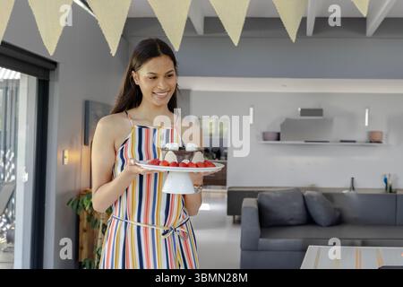 Frau hält Kuchenständer in moderner Küche mit Schokoladendessert, Erdbeeren, Kopierraum Stockfoto