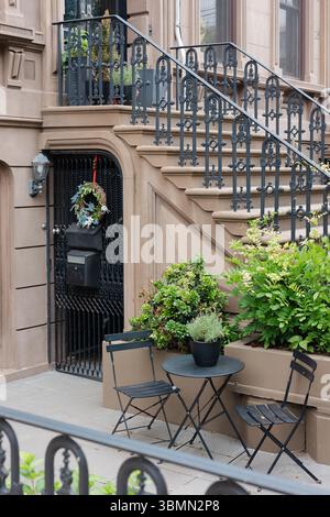 Gemütliche Sitzanordnung mit Pflanzen und einem Kranz in der Nähe eines stilvollen Sandsteineingangs in einer ruhigen Straße. Stockfoto