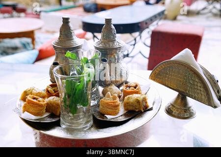 Pfefferminztee im arabischen Stil mit vier Stücken Hlou, tunesische Konditorei, serviert auf einem Silbertablett mit Silbertopf in einem tunesischen Café in Hammamet, T Stockfoto