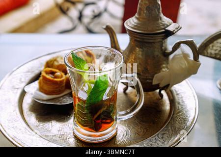 Pfefferminztee im arabischen Stil mit vier Stücken Hlou, tunesische Konditorei, serviert auf einem Silbertablett mit Silbertopf in einem tunesischen Café in Hammamet, T Stockfoto