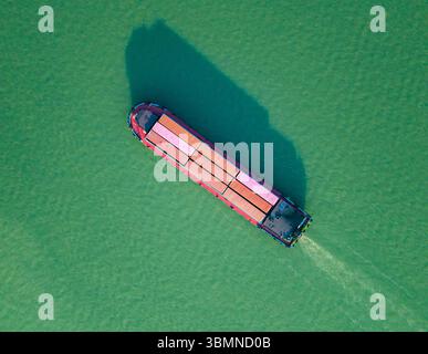 Luftaufnahme von oben nach unten auf das Containerschiff navigiert bei hellem Tageslicht in ruhigen Gewässern in der Nähe der Küste. Hangzhou, China. Stockfoto