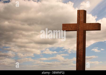 Ein flaches Holzkreuz steht am wolkigen Cumulushimmel und zeigt eine verwitterte Kornstruktur Stockfoto