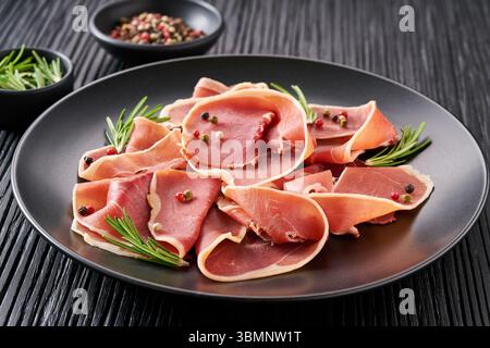 Italienischer Prosciutto Crudo oder Marmelade mit Rosmarin auf einem Teller auf einem schwarzen Holztisch. Stockfoto