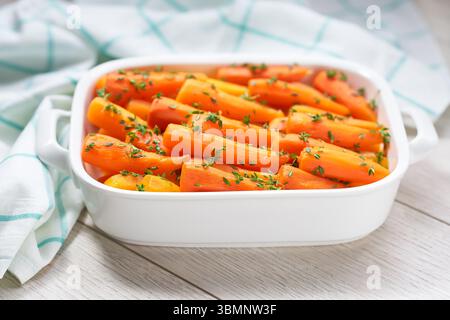 Gebackene BabyKarotten mit frischem Thymian in keramischer Form auf hellem Hintergrund. Gesundes Wurzelgemüse-Konzept. Stockfoto