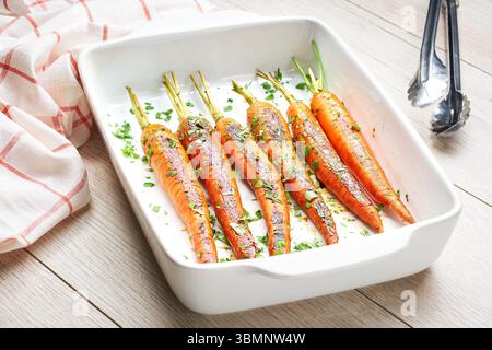 Gebratene Karotten mit frischer Petersilie in keramischer Form auf einem Holztisch. Gesundes Wurzelgemüse-Konzept. Stockfoto