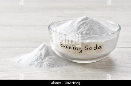 Backpulver in einer klaren Glasschale auf einem hellen Holztisch. Eine Glasschale mit Natriumbicarbonat auf einem weißen Holztisch. Stockfoto