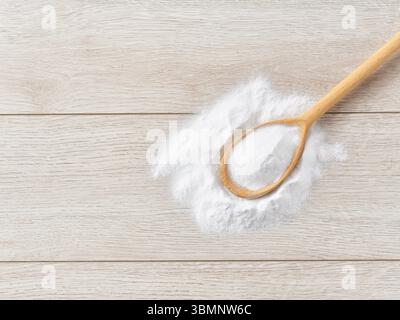 Natriumbicarbonat in einem Holzlöffel auf einem weißen Holztisch, mit Kopierraum für Text. Stockfoto