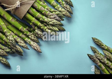 Ein Haufen essbarer, grüner Spargel, isoliert auf blauem Hintergrund. Frisches Gemüse, Draufsicht. Gesunde Mahlzeit. Frühlingsernte, landwirtschaftlicher Betrieb Stockfoto
