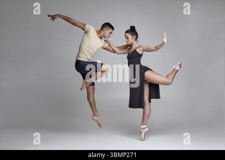Zwei junge kreative Balletttänzer posieren über einem grauen Studio-Hintergrund. Hübscher Mann in schwarzen Shorts mit beigem T-Shirt und schöner Frau in A Stockfoto