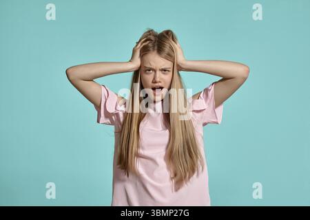 Studio-Porträt eines hübschen blonden Schulmädchens in einem rosa T-Shirt auf blauem Hintergrund in verschiedenen Posen. Sie drückt verschiedene Emotionen aus, die sich direkt darin posieren Stockfoto