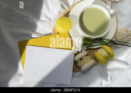 Weißes Papier Brief Kopie Raum Vorlage Süße gelbe Macaron Dessert Tasse grüner pflanzlicher Matcha Tee Latte in gemütlicher Morgen Bett Atmosphäre. Kreativ Stockfoto
