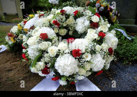 Repräsentativer weißer Trauerkranz mit Hortensien, Rosen, Gänseblümchen, gypsophila und einigen roten Rosen auf einem Grab nach einer Beerdigung Stockfoto