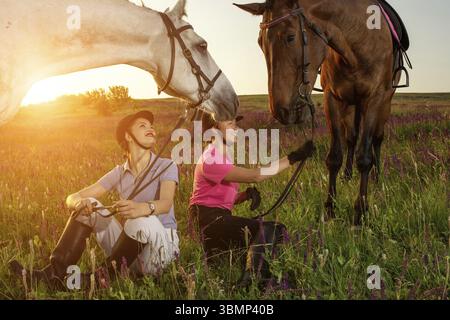 Zwei Frauen und zwei Pferde draußen im Sommer glücklicher Sonnenuntergang zusammen Natur. Tierpflege, Liebes- und Freundschaftskonzept Stockfoto