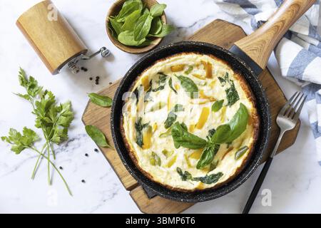 Spinat und Käseomelette. Frittata aus Eiern, Paprika und Spinat in einer Pfanne auf einer Marmorplatte. Blick von oben Stockfoto