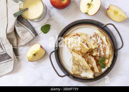 Pancake Day feiern, gesundes Frühstück. Hausgemachte süße Crepes mit Äpfeln und Kondensmilch auf einer Marmorplatte. Draufsicht flach Stockfoto