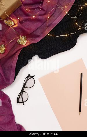 Schwarze Gläser, rosa Papier mit neuen Jahren Ziele. Schal und Weihnachtsbeleuchtung auf weißem Hintergrund. Ansicht von oben. Kopieren Sie Platz. Immer noch leben. Flach Stockfoto
