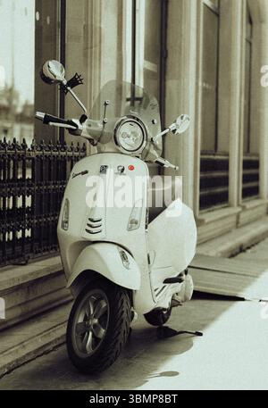 Klassischer weißer Vespa-Roller, der auf einem Bürgersteig der Stadt geparkt ist, vermittelt ein Gefühl von urbaner Mobilität und Stil Stockfoto