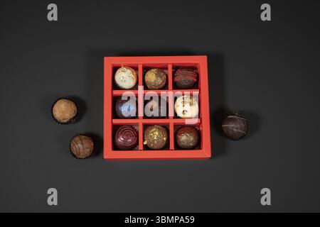 Verschiedene handgemachte Schokoladentrüffel-Bonbons in einer roten Box auf dunklem Hintergrund. Direkt über Draufsicht Stockfoto
