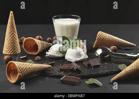 Nahaufnahme mit köstlichem Creme- und Schokoladeneis dekoriert mit Minze, einem Glas Milch, Eiswürfeln, Metallkugel, Waffelkegel mit Schokolade und Stockfoto