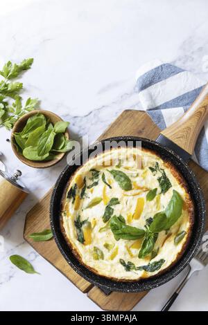 Spinat und Käseomelette. Frittata aus Eiern, Paprika und Spinat in einer Pfanne auf einer Marmorplatte. Blick von oben. Kopierbereich Stockfoto