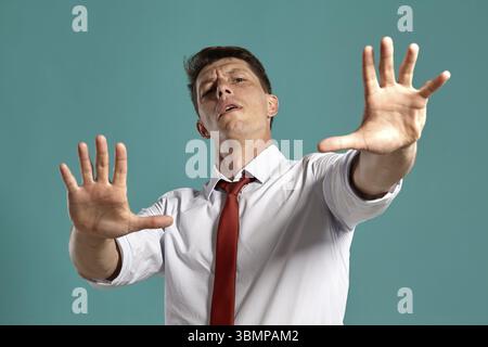 Studio-Porträt eines prächtigen jungen Mannes in klassischem weißem Hemd und roter Krawatte, der sich wie ein Stoppen über einem blauen Hintergrund benimmt. Taststift Stockfoto