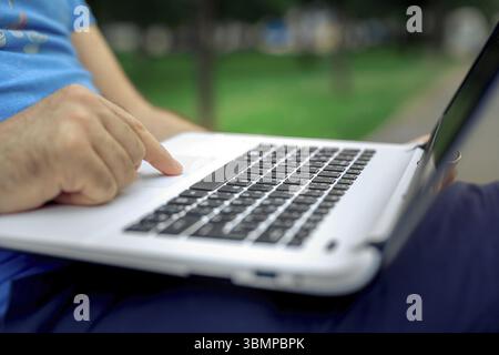 Nahaufnahme der Hände eines gutaussehenden Mannes, der den Bildschirm des Laptops berührt. Geschäftsmann, der einen Laptop benutzt und auf dem Boden sitzt Stockfoto