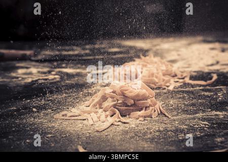 Home frische rohe Pasta auf dem Küchentisch schwarzen Beton, bestreuen mit Mehl. Foto in Brauntönen Stockfoto
