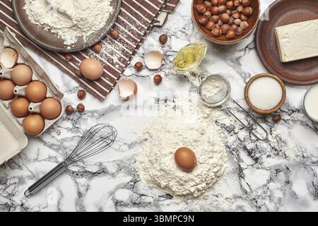 Blick von oben auf Backzutaten und Küchenutensilien auf Marmorhintergrund. Es gibt ein paar Eier und eine Eierschale, Mehl auf einem Teller, der auf einem braunen Str. steht Stockfoto