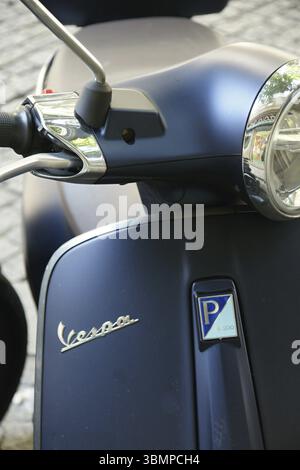 Glänzender Chrom-Lenker und Scheinwerfer eines dunkelblauen Vespa-Rollers, der auf einer kopfsteingepflasterten Straße geparkt ist und sein ikonisches Design zeigt Stockfoto