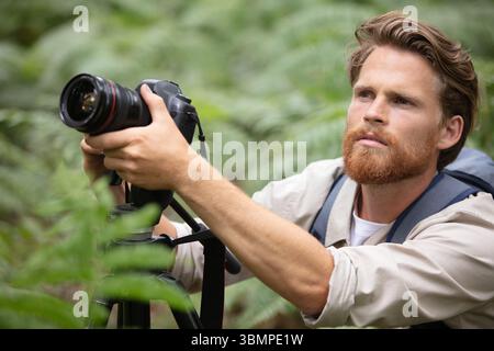 Ein Mann mit Bart hält eine Fotokamera auf die grüne Natur Stockfoto