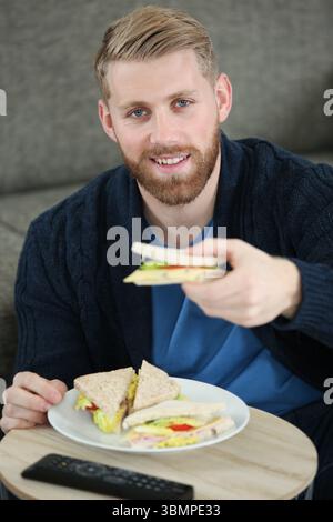 Junger Mann, der zu Hause leckeres Sandwich isst Stockfoto