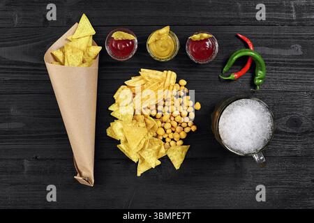 Blick von oben auf Bierglas und Snacks mit Sauce auf schwarzem Holztisch. Draufsicht. Speicherplatz kopieren. Stillleben. Flach liegend Stockfoto
