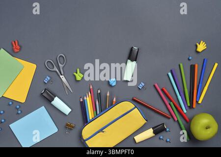 Flachbild-Foto eines Arbeitsplatzes mit Schulzubehör wie Filzstiften, Filzstiften, Scheren, Radiergummis, einem Apfel, Knöpfe, gelbes Bleistiftetui, Stockfoto