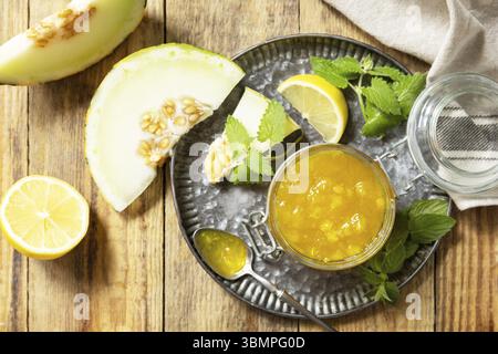 Süße Melonen- und Zitrusmarmelade oder Gelee in einem kleinen Glas mit frischen Melonenscheiben auf rustikalem Holztisch. Hausgemachtes Preserve. Blick von oben Stockfoto