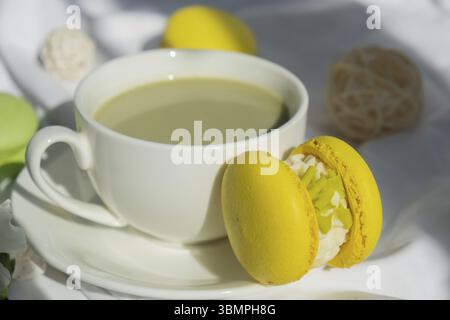 Süßes gelbes Macaron Dessert Tasse grüner Matcha Tee Latte auf Pflanzenbasis in gemütlicher Morgenliegenatmosphäre. Kreative Urlaubsidee mit romantischem Date. Pflanzliche Präparate Stockfoto
