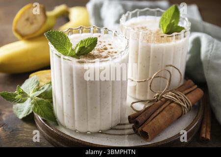 Bananen-Smoothie mit Zimt in Trinkglas auf hölzernem Hintergrund. Entgiftungsmenü Stockfoto