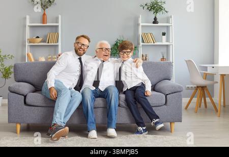 Glücklicher Vater, Sohn und Großvater in weißen Hemden und schwarzen Krawatten sitzen auf der Couch und umarmen sich. Stockfoto