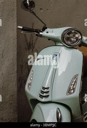 Nahaufnahme eines hellgrünen Vespa-Rollers, der in der Nähe einer Betonmauer geparkt ist und sein Design zeigt Stockfoto