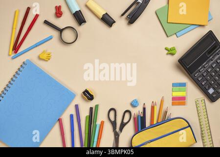 Helles, flaches Foto eines Arbeitsplatzes mit Schulutensilien wie blauem Notizbuch, farbigen Bleistiften, gelbem Bleistiftetui, zwei Markierungen, Filzstiften Stockfoto