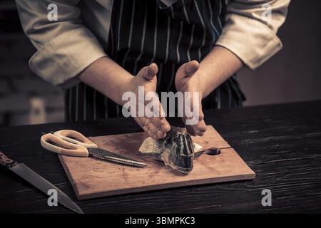 Koch schneidet den Fisch auf einem Brett. Foto in Brauntönen. Küche. Holztisch Stockfoto