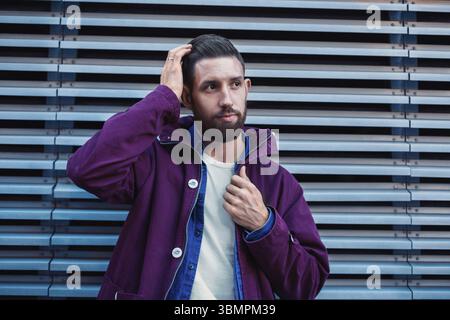 Hübscher junger Mann mit Frisur in modische Kleidung steht in der Nähe der Eisernen Mauer und seitwärts. Street fashion Stockfoto